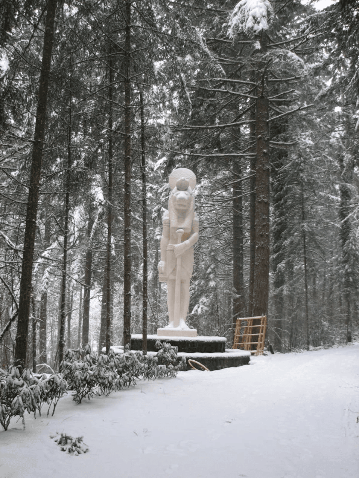 A white Sekhmet statue standing on a pedestal in a snow-covered forest