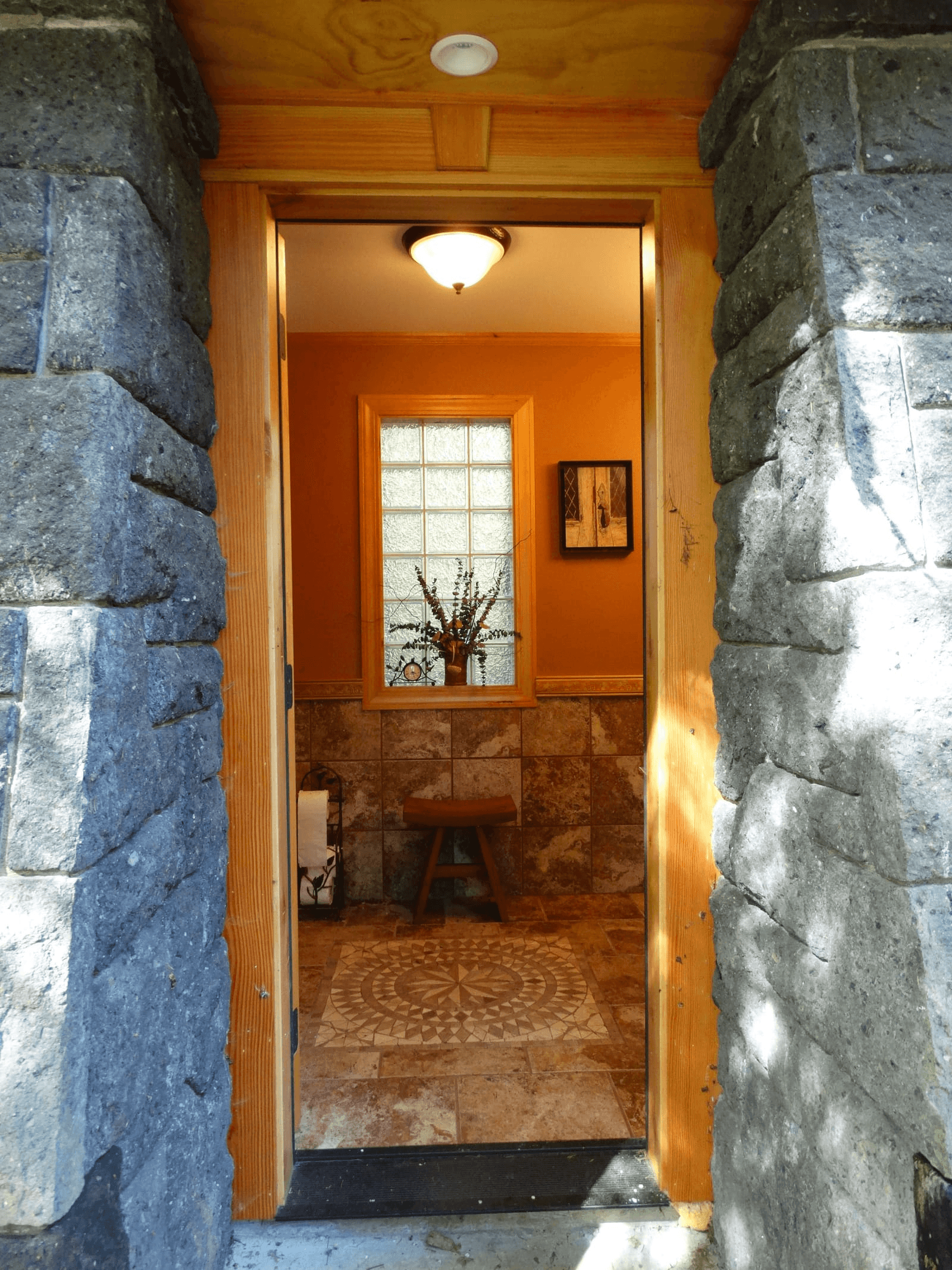 A doorway through a stone wall opening into a small tiled room with a mosaic floor